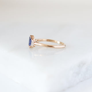 Blue emerald cut sapphire and diamond ring on white background, half view