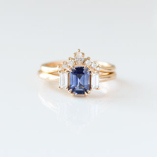 Blue emerald cut sapphire and diamond ring on white background with curved diamond wedding band, front view