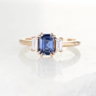 Blue emerald cut sapphire and diamond ring on white background 
