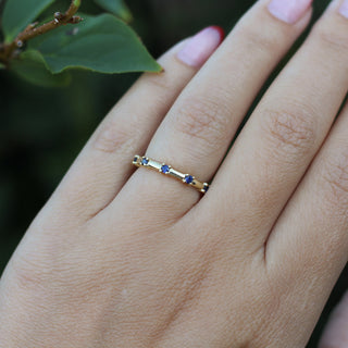 Gold ring with blue stones on a person's finger against a blurred green background