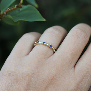 Gold ring with blue stones on a finger against a green leafy background