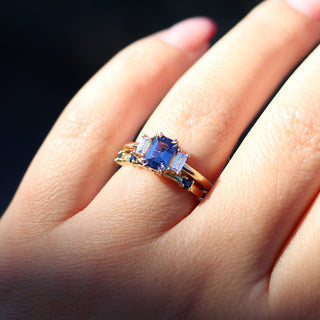 Yellow gold ring with blue gemstone on a hand against a dark background