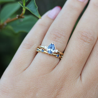 Gold ring with a blue gemstone on a hand against a blurred green background