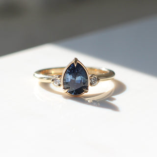 Three stone engagement ring with a blue pear cut sapphire in yellow gold, front view