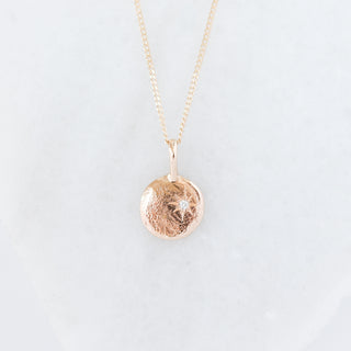 Gold necklace with a round pendant on a light gray background
