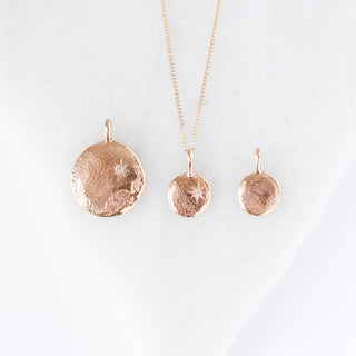 Three yellow gold necklaces with textured pendants on a white background