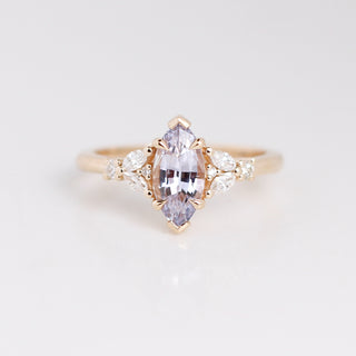 Yellow gold ring with a central purple sapphire and smaller diamonds on a light grry background