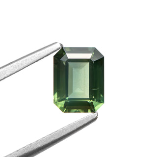Green emerald cut sapphire on white background, held by tweezers