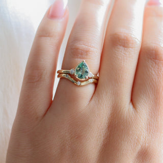 Three stone engagement ring with a green pear cut sapphire in yellow gold stacked with a curved three diamond wave band, on hand