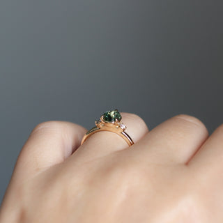Three stone engagement ring with a green pear cut sapphire in yellow gold, side view on hand