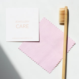 A jewellery cleaning kit with a pink polishing cloth, a recyclable bamboo brush, and a card reading 'JEWELLERY CARE'.