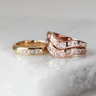 Custom waved wedding bands with ethically sourced diamonds in rose gold settings, handcrafted by Yuliya Chorna at her Toronto studio.