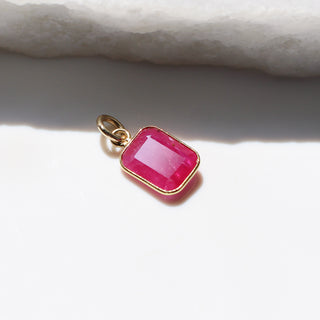 Large Ruby Bezel Charm beside marble slab casting shadows from bring sunlight detailed side view