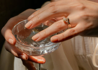 Close-up of hands wearing gold rings and holding a glass with a blurred background
