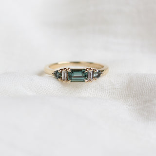 Yellow gold ring with a teal green emerald cut sapphire, front view