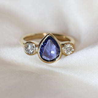 three stone engagement ring in yellow gold with a pear shaped blue sapphire framed by two round white diamonds