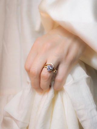 pear shaped gemstone ring in yellow gold with diamond band on hand against light satin fabric