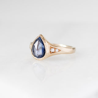 Yellow gold ring with a blue teardrop gemstone on a light grey background