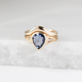 Gold ring with a pear-shaped blue gemstone and gold band on a light grey background