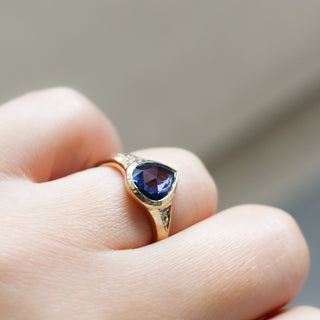 Gold ring with a blue gemstone on a finger against a neutral background