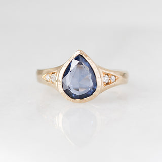 Gold ring with a blue teardrop-shaped gemstone on a light gray background