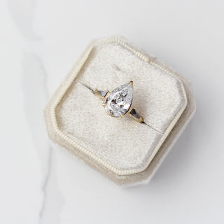 Pear shaped diamond ring in a hexagonal box on a light grey background