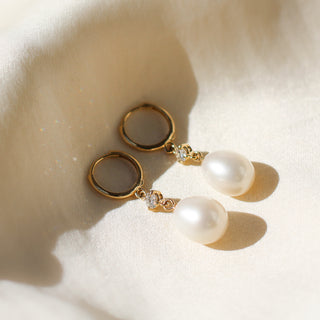 Pearl and diamond drop hoop earrings lying on white fabric. side view