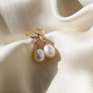 Pearl and diamond drop hoop earrings lying on white fabric, front view