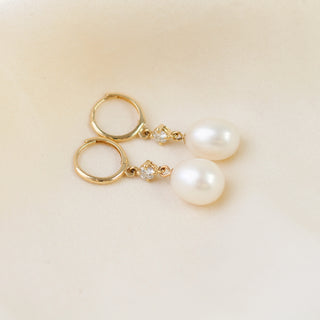 Pearl and diamond drop hoop earrings lying on white fabric, side view