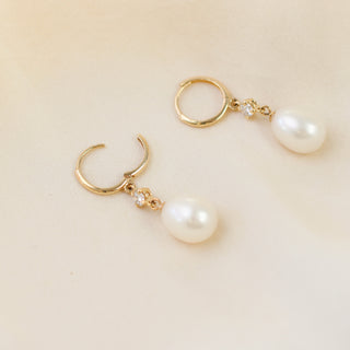 Pearl and diamond drop hoop earrings lying on white fabric with open hoops, quarter view