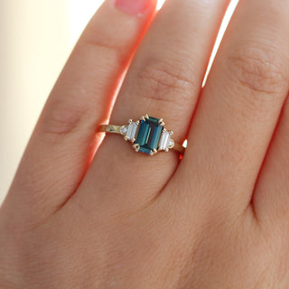 Ring with teal gemstone and diamonds on a hand against a neutral background