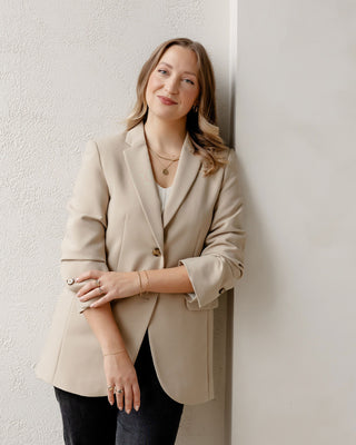 Founder Yuliya Chorna standing in a beige blazer and wearing fine jewellery hand crafted in her Toronto studio.