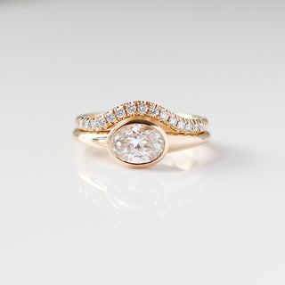 Yellow gold ring with a bezel set white oval cut diamond with a curved yellow gold wedding band with round white diamonds, front view