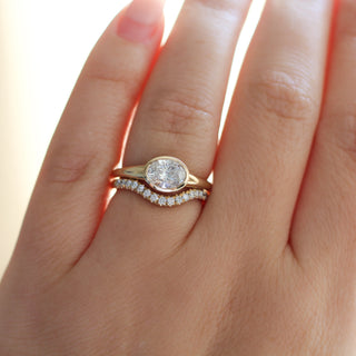 Yellow gold ring with a bezel set white oval cut diamond with a curved yellow gold wedding band with round white diamonds, on hand