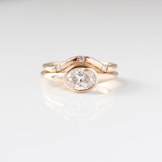 Yellow gold ring with a bezel set white oval cut diamond with a curved yellow gold wedding band with round white diamonds, front view