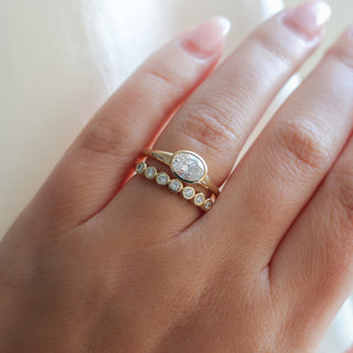 Yellow gold ring with a bezel set white oval cut diamond with a straight yellow gold wedding band with bezel set round white diamonds, on hand