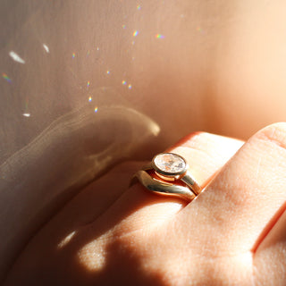 Yellow gold ring with a bezel set white oval cut diamond with a curved yellow gold wedding band, on hand