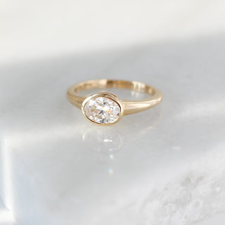 Yellow gold ring with a bezel set white oval cut diamond, front view
