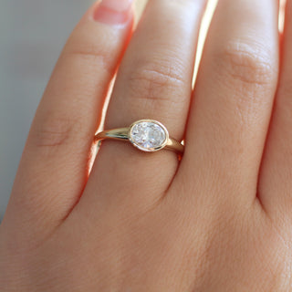 Yellow gold ring with a bezel set white oval cut diamond, on hand
