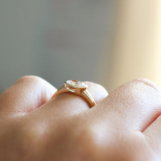 Yellow gold ring with a bezel set white oval cut diamond, on hand, side view