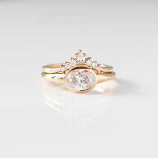 Yellow gold ring with a bezel set white oval cut diamond with a curved yellow gold wedding band with round white diamonds, front view