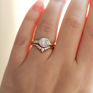 Yellow gold ring with a bezel set white oval cut diamond with a curved yellow gold wedding band with round white diamonds, on hand