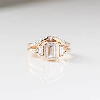 Yellow gold ring with a bezel set white emerald cut diamond and four white diamond accents with a yellow gold wedding band with round white diamonds, front view