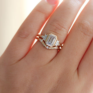 Yellow gold ring with a bezel set white emerald cut diamond and four white diamond accents with a yellow gold wedding band with round white diamonds, on hand