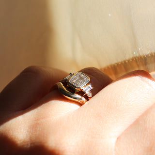 Yellow gold ring with a bezel set white emerald cut diamond and four white diamond accents with a yellow gold wedding band, on hand quarter view