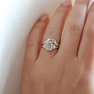 Yellow gold ring with a bezel set white emerald cut diamond and four white diamond accents with a yellow gold wedding band with assorted white diamonds, on hand