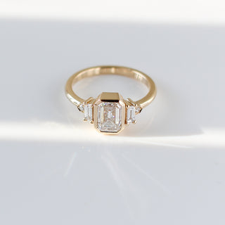 Yellow gold ring with a bezel set white emerald cut diamond and four white diamond accents, quarter view from above