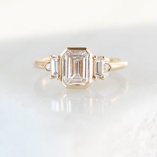 Yellow gold ring with a bezel set white emerald cut diamond and four white diamond accents, front view