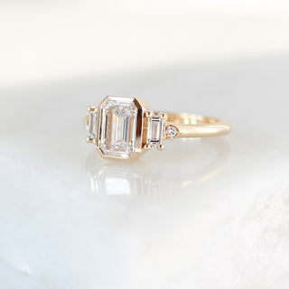 Yellow gold ring with a bezel set white emerald cut diamond and four white diamond accents, quarter view
