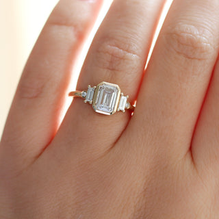 Yellow gold ring with a bezel set white emerald cut diamond and four white diamond accents, on hand